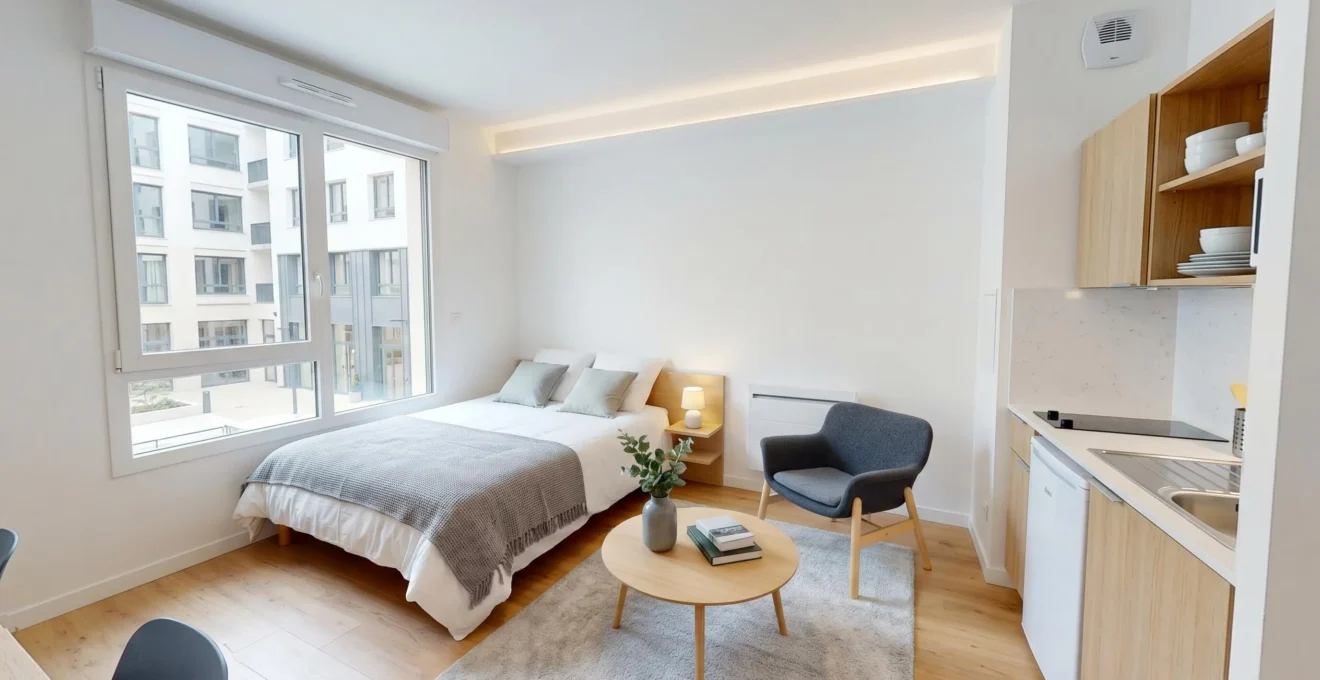 Intérieur d'un studio meublé contemporain montrant les composants amortissables : structure (murs, fenêtre), équipements (radiateur, VMC), mobilier (lit, table, cuisine équipée)